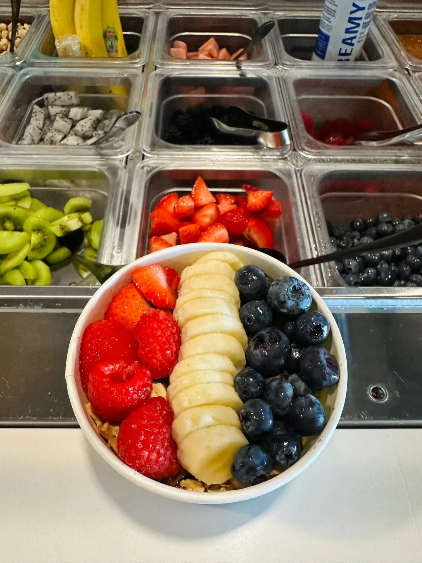 Açaí bowl with raspberries, strawberries, banana and blueberries beside the fresh fruit bar