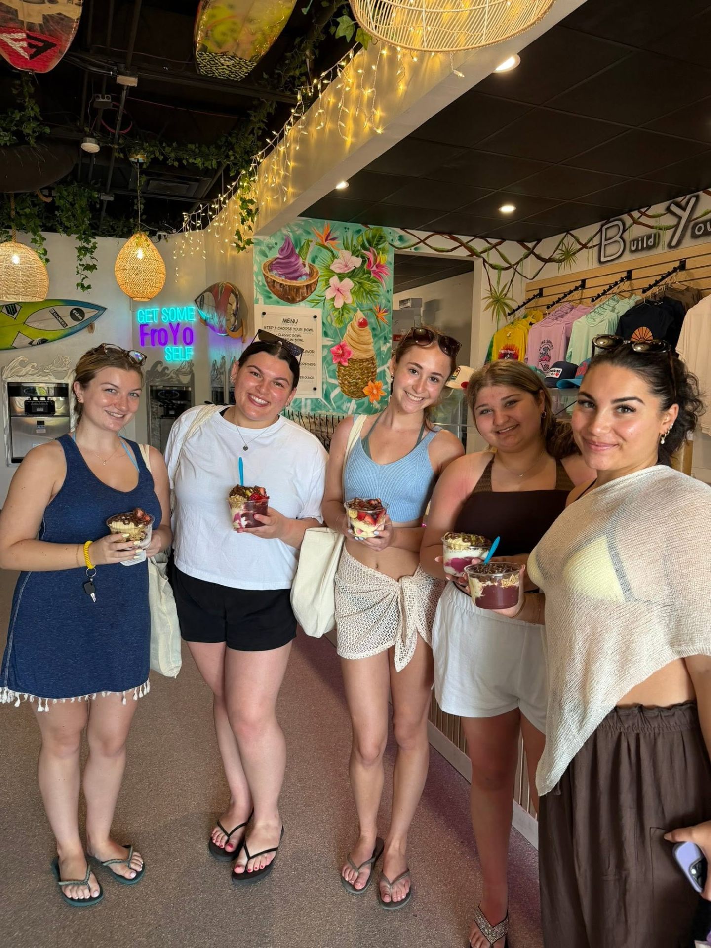Five girls smiling with froyo cups under the neon Get Some FroYo Self sign