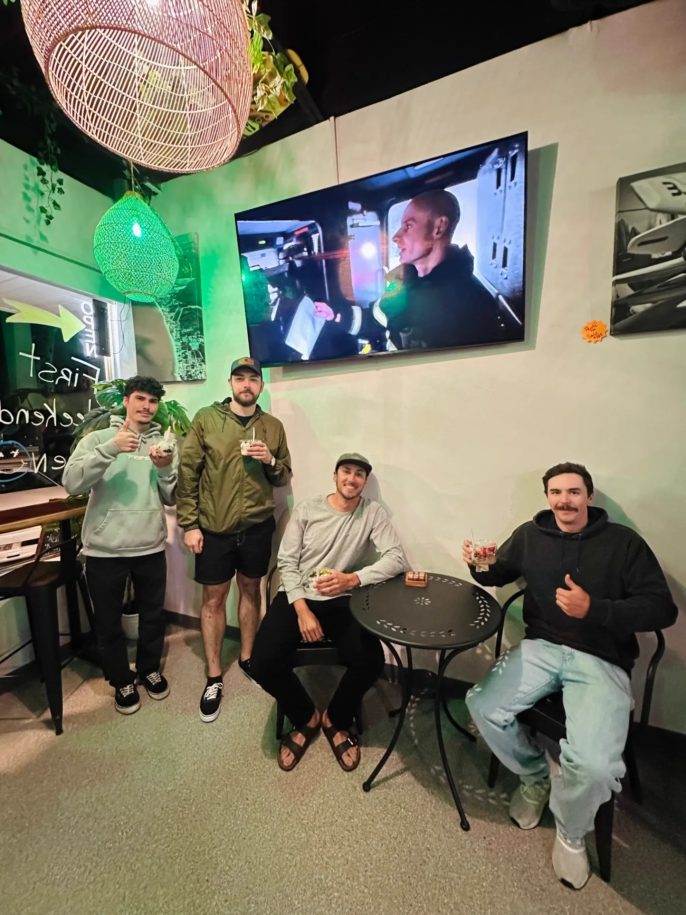 Four friends with froyo cups hanging out under the TV at AMI FroYo