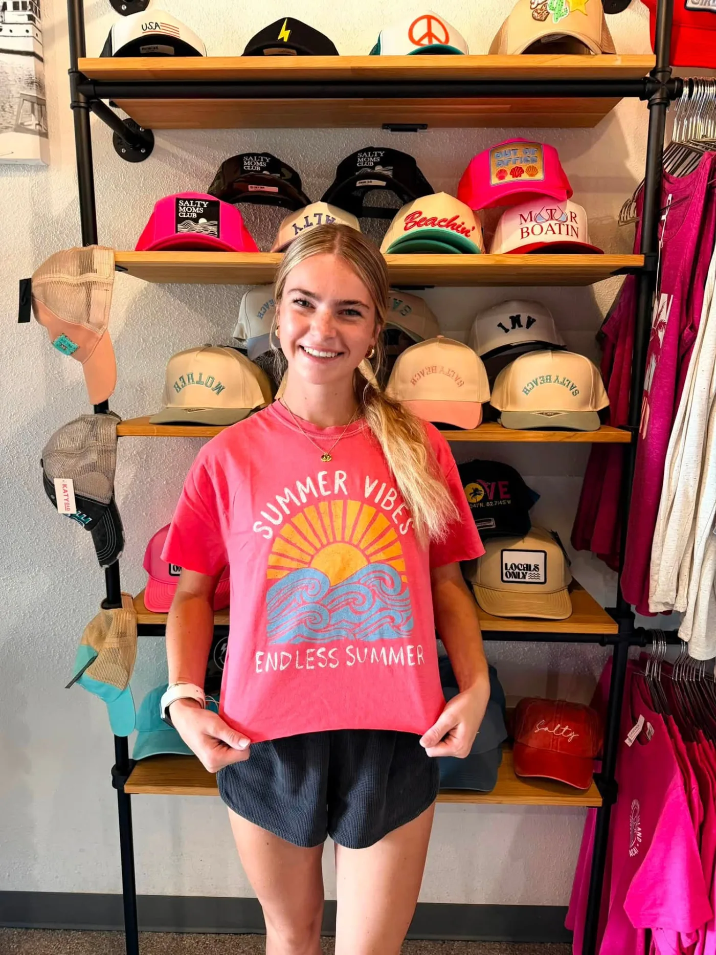 Staff member in a Summer Vibes tee in front of the trucker hat wall at AMI FroYo