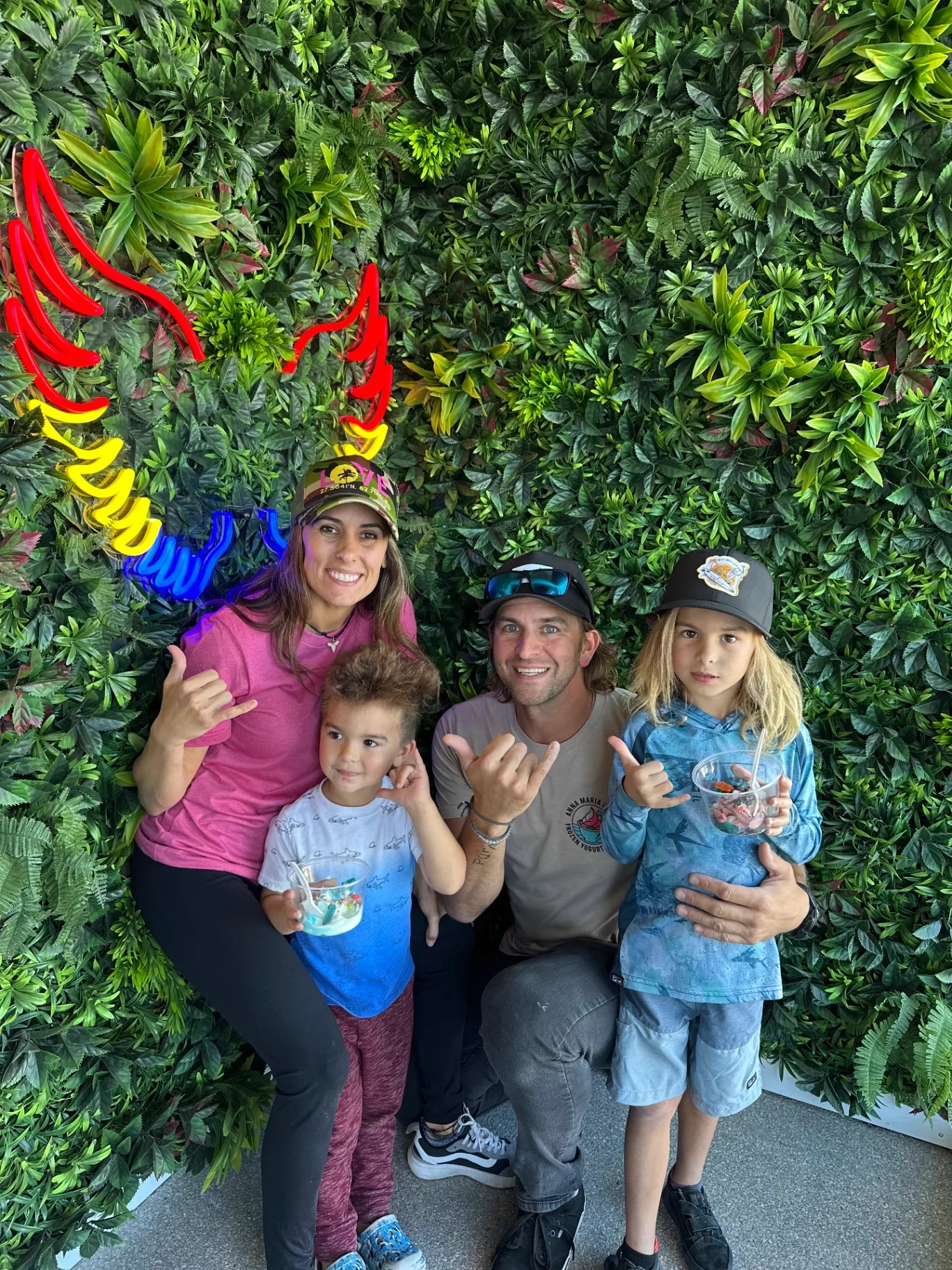Family with froyo bowls in front of the green plant wall at AMI FroYo
