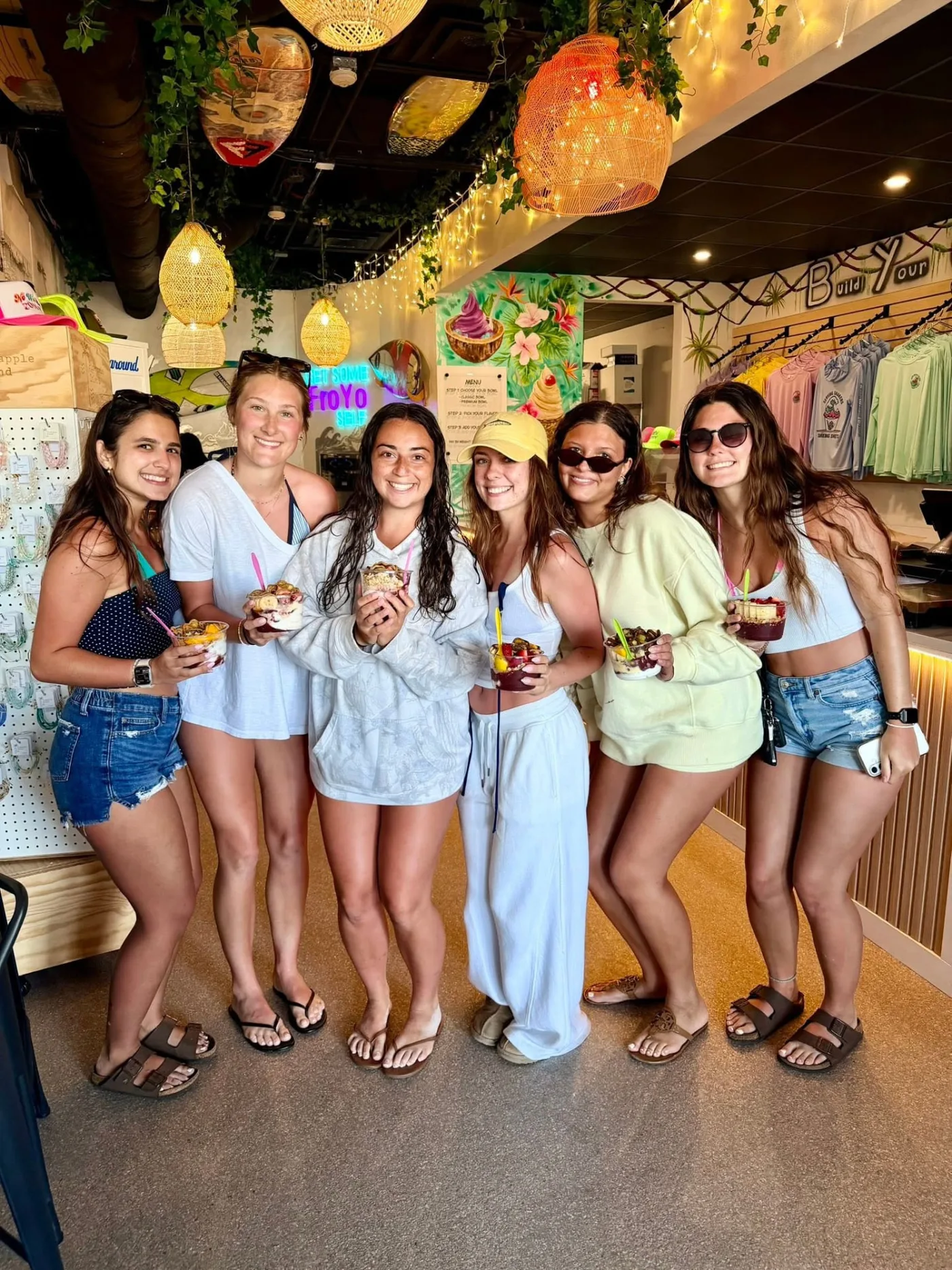 Six friends holding froyo and açaí bowls inside AMI FroYo under the rattan lights